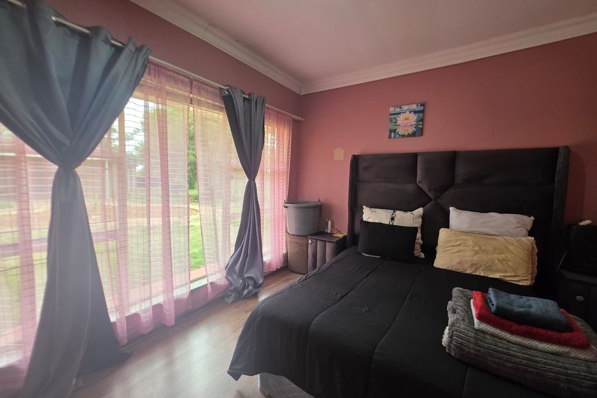 A bedroom featuring laminate flooring, cove cornicing, and a large window allowing natural light into the space.