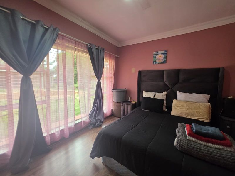 A bedroom featuring laminate flooring, cove cornicing, and a large window allowing natural light into the space.