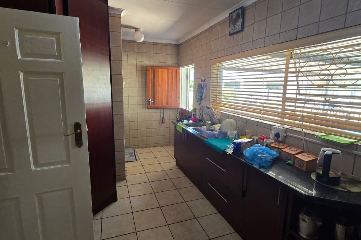 A functional kitchen featuring dark wood cabinetry, granite countertops, tiled splashbacks, and tiled flooring, offering a practical layout with ample natural light.