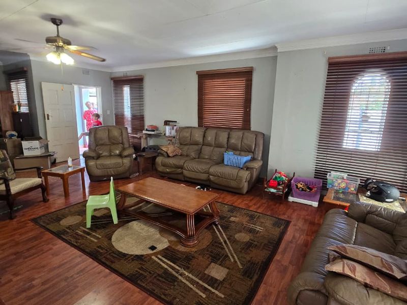 Spacious living room featuring laminate flooring, ceiling fan, and large windows with wooden blinds, offering a comfortable and functional family living space.