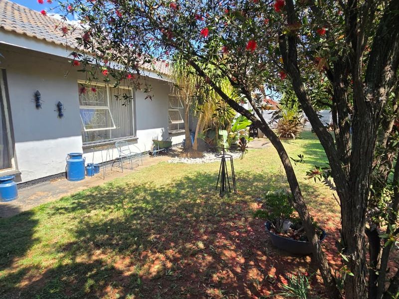 A view of the rear garden featuring a lawn, mature trees, and the rear facade of the house with tiled roofing and casement windows.