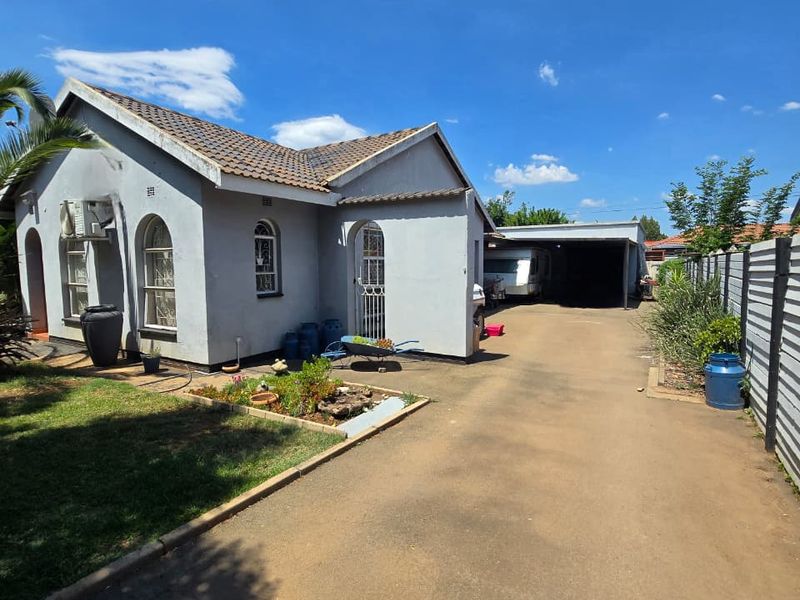 Front view of a single-story house featuring arched windows, a tiled roof, a long paved driveway, and a covered carport area.