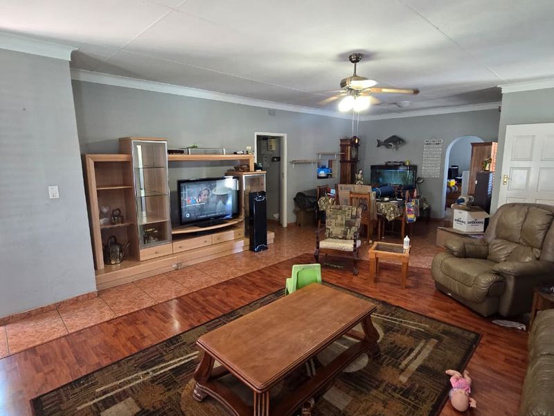 Spacious living area featuring a combination of laminate and tiled flooring, ceiling fan, and coved cornicing, requiring some ceiling maintenance.
