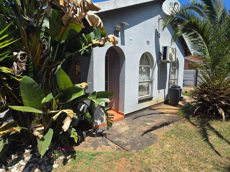 Rear exterior view of the house featuring arched windows, a wall-mounted air conditioning unit, and a paved walkway area.