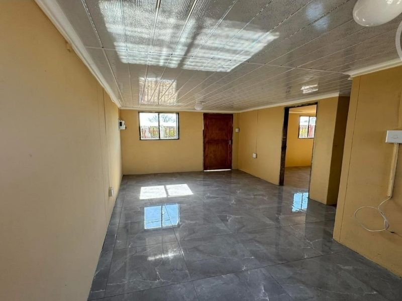 An empty living area featuring grey tiled flooring, PVC ceiling panels, and natural light through aluminium-framed windows.