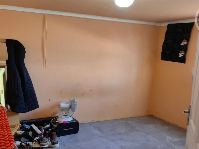 A bedroom featuring tiled flooring and coving, currently showing signs of wear including scuffed and peeling wall paint.