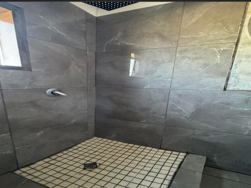 A shower enclosure featuring large format grey wall tiles and mosaic floor tiling, currently showing signs of incomplete finishing.