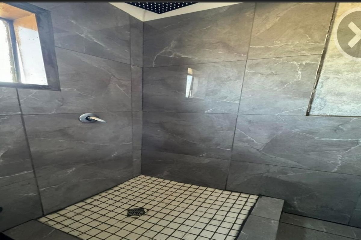 A shower enclosure featuring large format grey wall tiles and mosaic floor tiling, currently showing signs of incomplete finishing.
