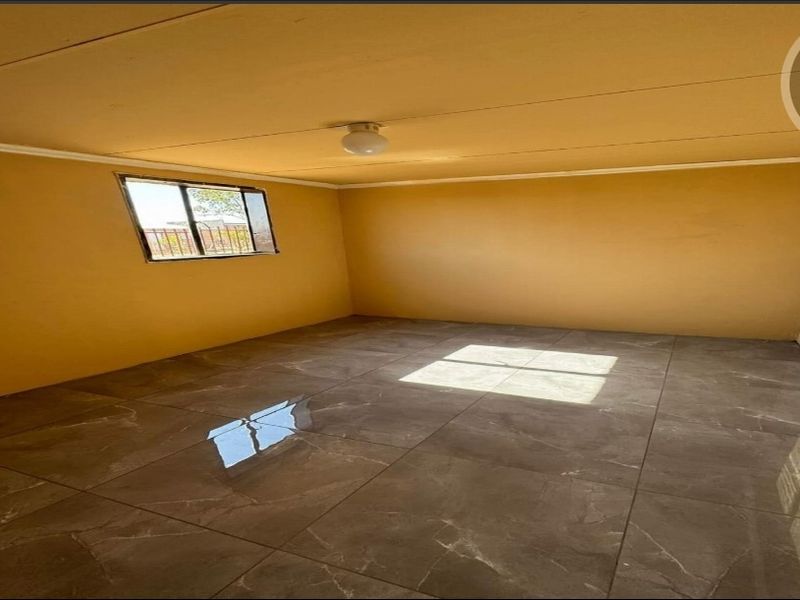 A clean, empty bedroom featuring modern large-format floor tiles, neutral wall paint, and a window fitted with security bars.