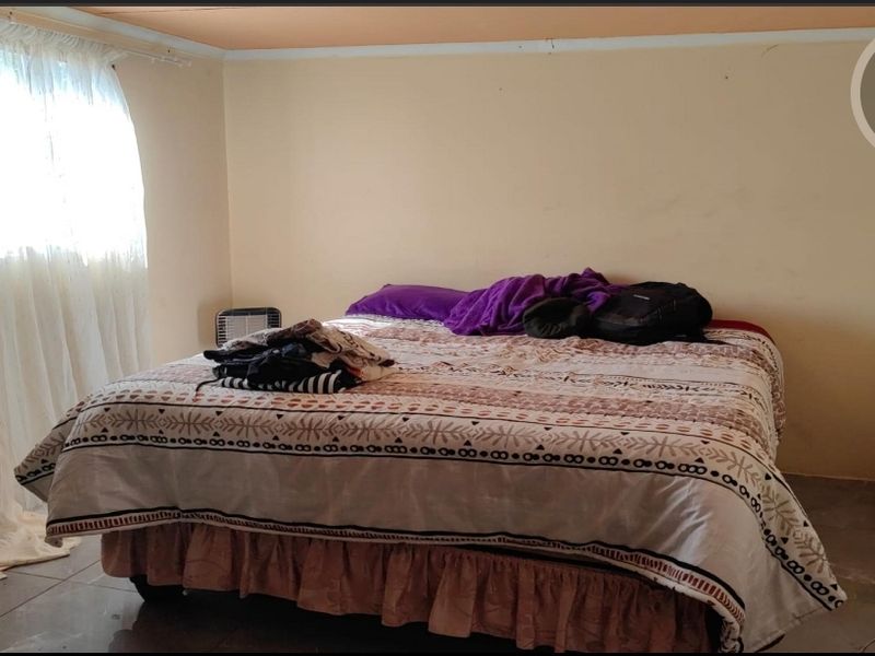 A simple bedroom featuring tiled flooring and a window with curtains, requiring cosmetic updates to improve the overall aesthetic and finish.