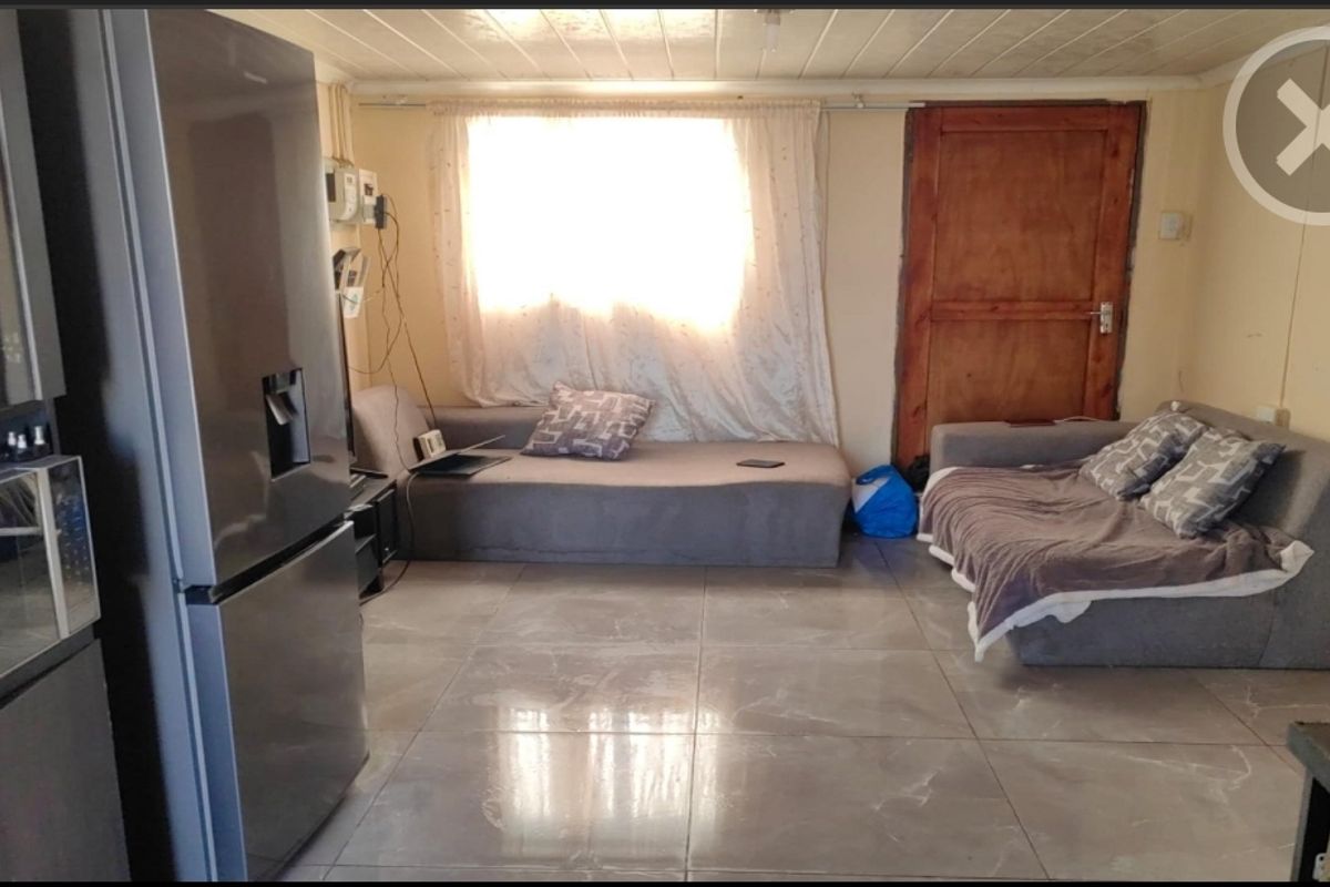 A living area featuring large format floor tiles, a timber door, and a window, currently used as a multi-purpose living space.