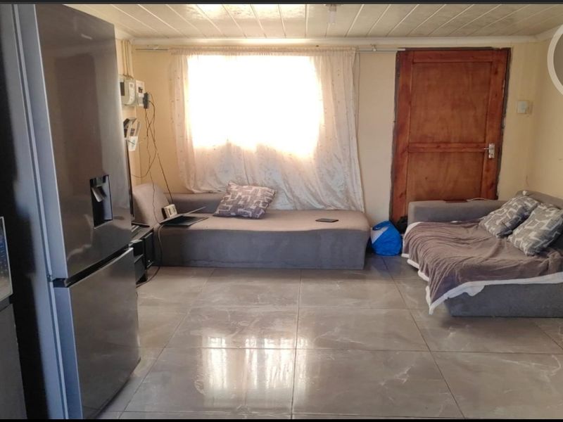 A living area featuring large format floor tiles, a timber door, and a window, currently used as a multi-purpose living space.