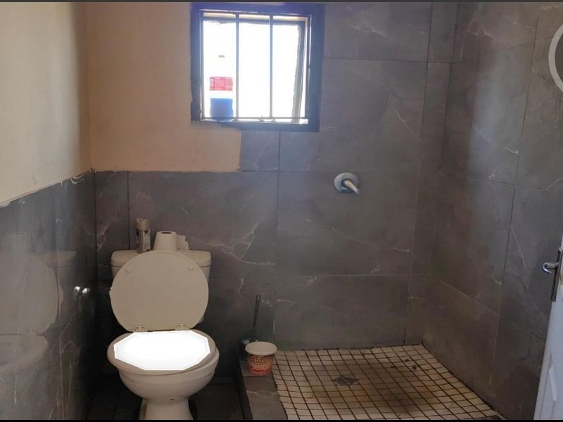 A small bathroom featuring grey wall tiles, a toilet, and a shower area. The space requires finishing touches to the wall tiling and paintwork.
