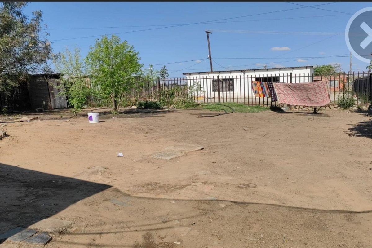 A spacious rear yard area featuring metal perimeter fencing and an outbuilding, offering significant potential for landscaping and outdoor development.