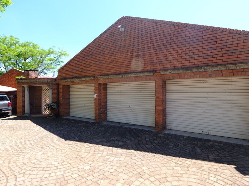 A spacious triple garage featuring classic brick construction and secure roller shutter doors, complemented by a well-maintained paved driveway.