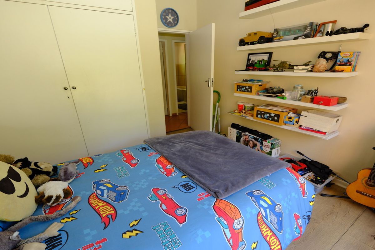 A functional bedroom featuring built-in cupboards, floating wall shelving, and durable laminate flooring, providing a practical space with ample storage options.