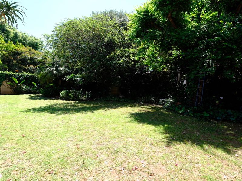 A spacious, well-established garden featuring a large lawn area surrounded by mature trees and lush greenery.