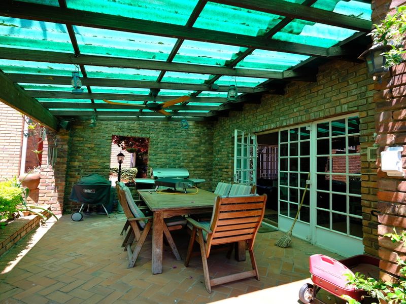 Covered outdoor patio area featuring exposed brick walls, herringbone brick flooring, and a timber pergola structure with a translucent roof.