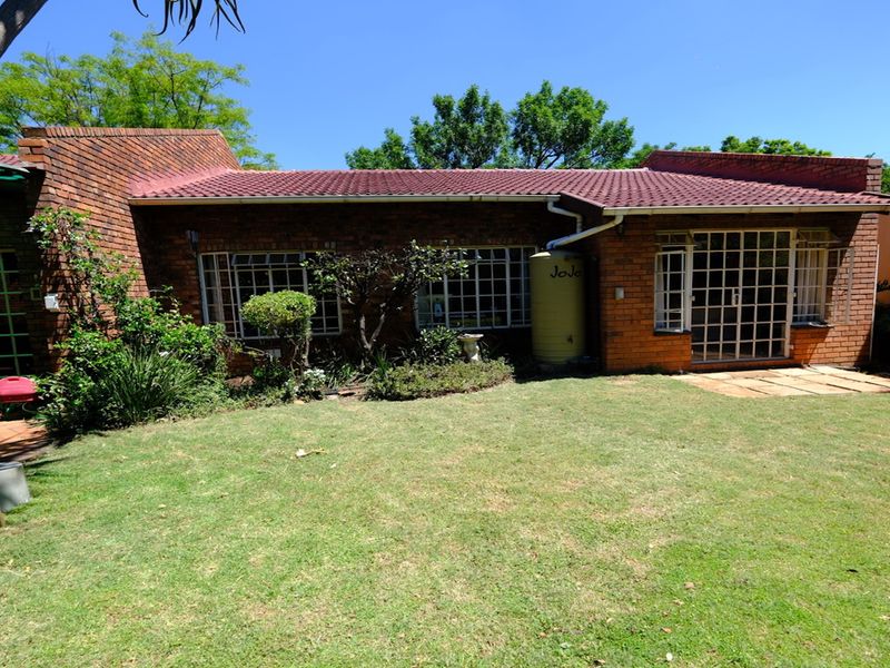 Rear view of a face brick house featuring a tiled roof, security bars on windows, and a water tank set within a private garden.