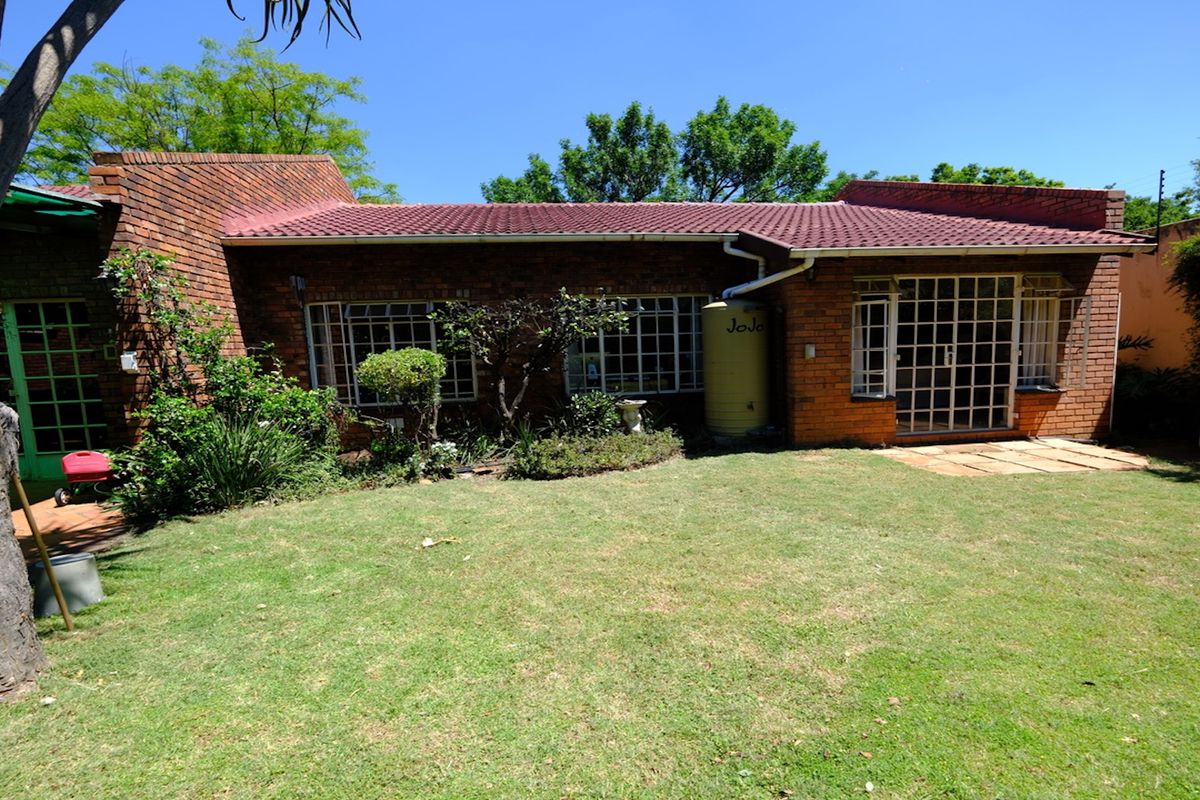 Rear view of a face brick house featuring a tiled roof, security bars on windows, and a water tank set within a private garden.