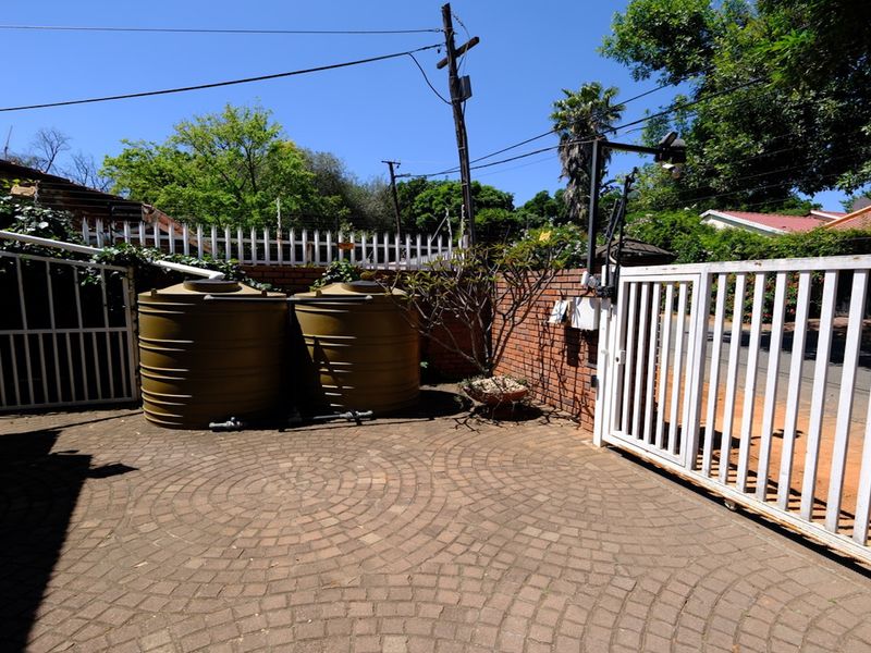 Front entrance area featuring a paved driveway, secure metal gate, and installed water storage tanks against a brick boundary wall.