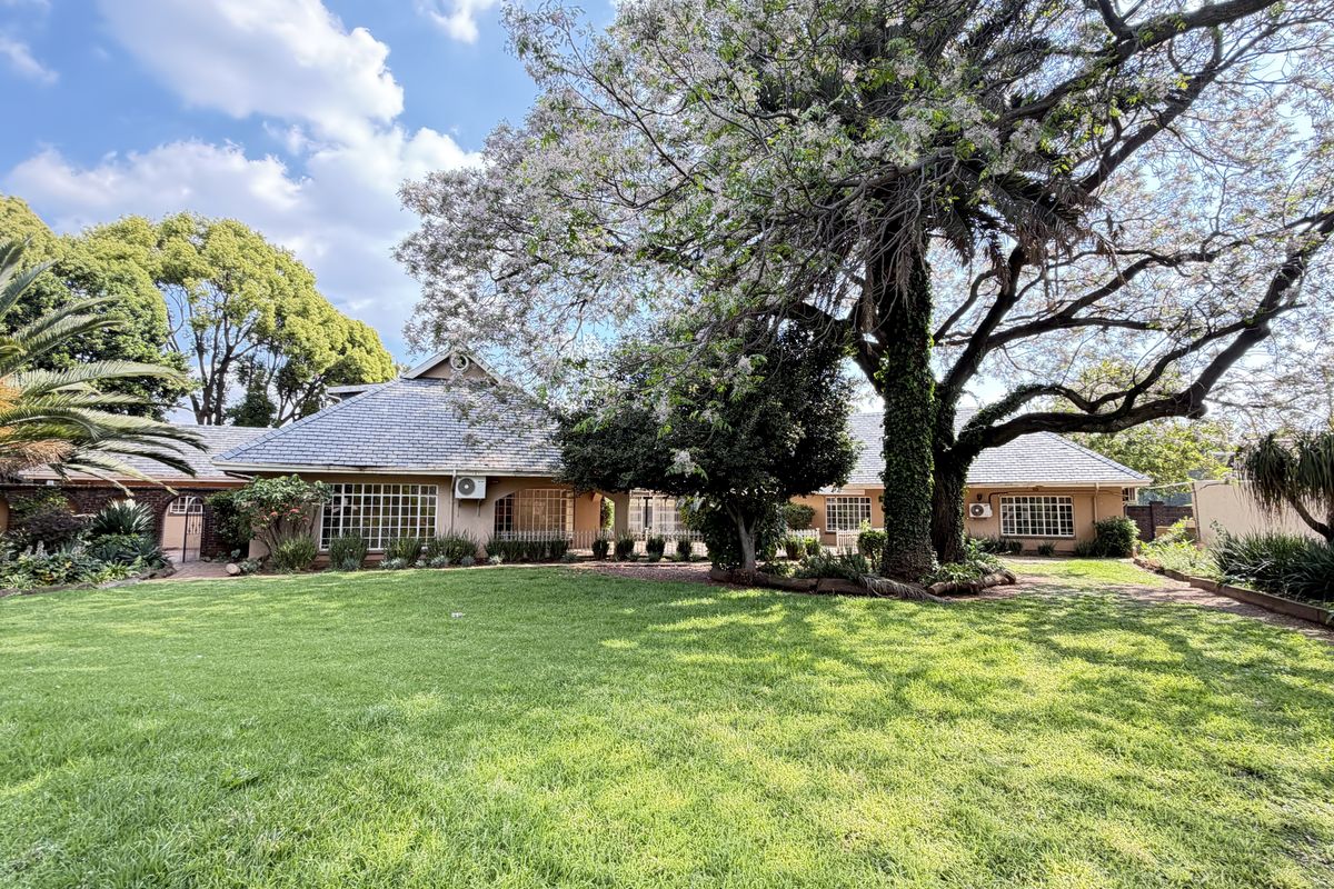 A spacious rear garden featuring a well-maintained lawn, mature trees, and a view of the house exterior with tiled roofing and grid-pattern windows.