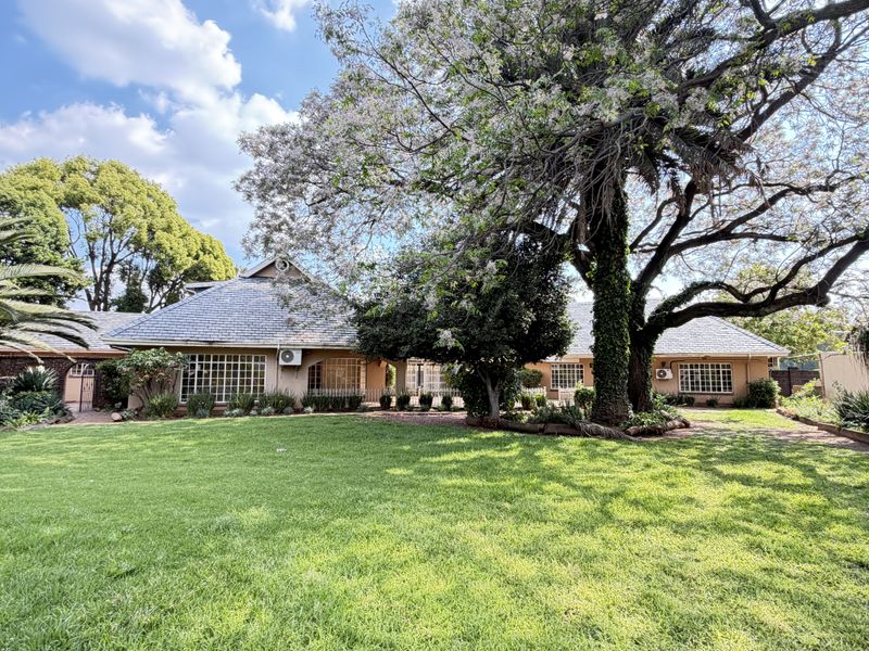 A spacious rear garden featuring a well-maintained lawn, mature trees, and a view of the house exterior with tiled roofing and grid-pattern windows.