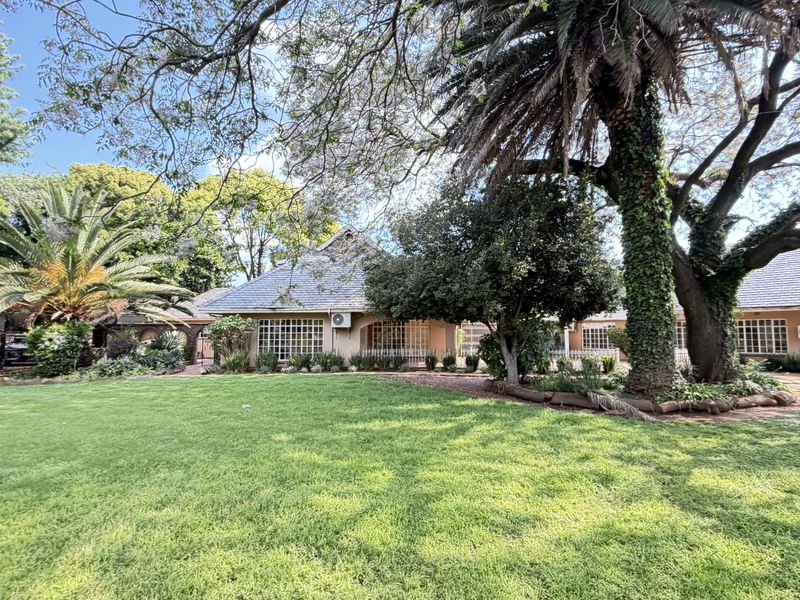 A spacious rear garden featuring a well-maintained lawn, mature trees, and a view of the house exterior with tiled roofing and security-fitted windows.