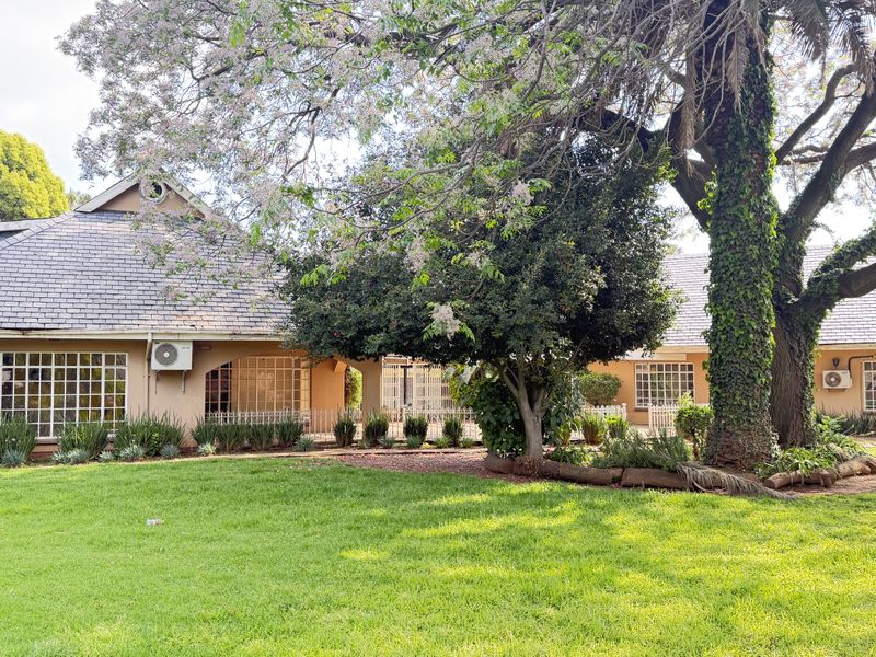 A view of the rear elevation featuring a well-maintained garden, mature trees, and a tiled roof with grid-pattern windows.