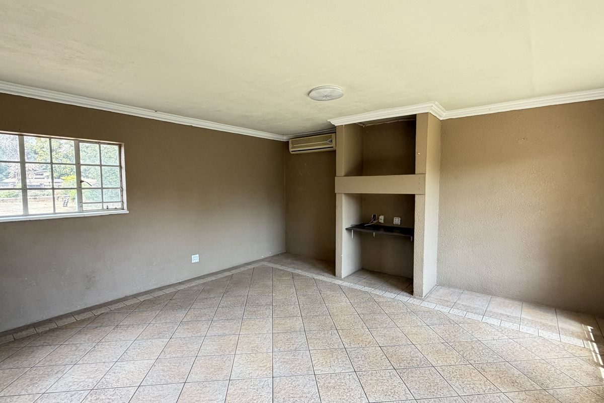 An empty living room featuring tiled flooring, a built-in wall niche, and a wall-mounted air conditioning unit.