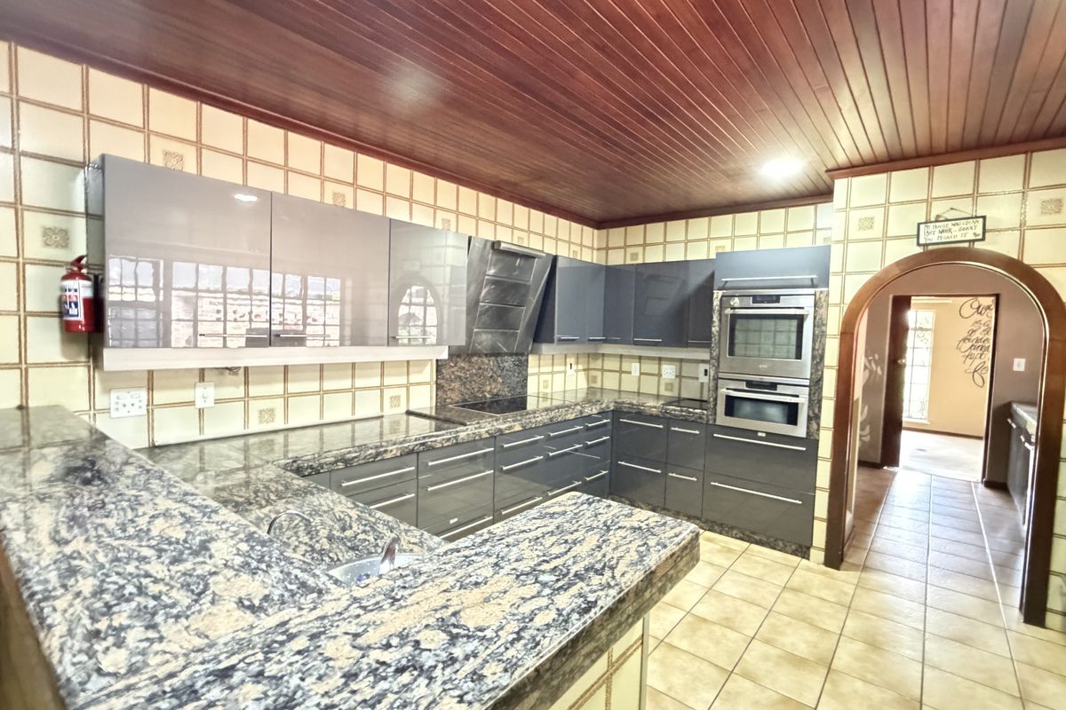 A functional kitchen featuring granite countertops, built-in stainless steel appliances, a timber ceiling, and classic ceramic wall and floor tiling.