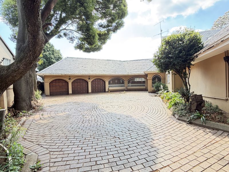Spacious front exterior featuring a large paved circular driveway and a triple garage with arched wooden doors.