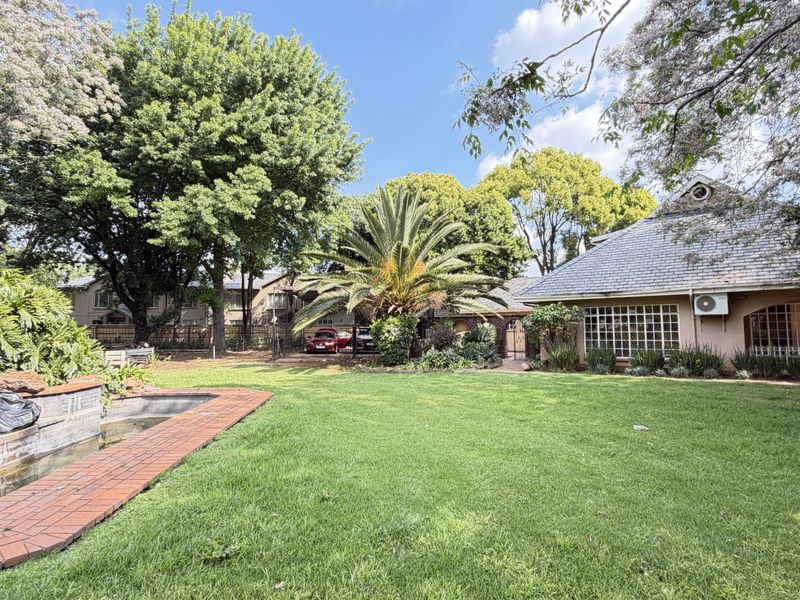 Spacious rear garden featuring a large lawn, mature trees, and a brick-lined water feature adjacent to the main house structure.