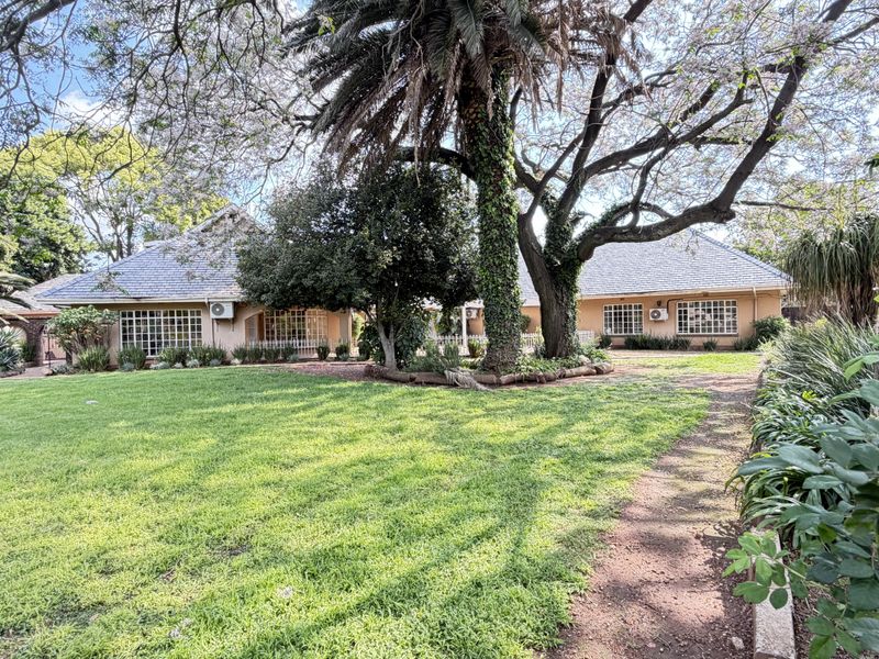 A spacious rear garden featuring a well-maintained lawn, mature trees, and a view of the house exterior with tiled roofing and air conditioning units.