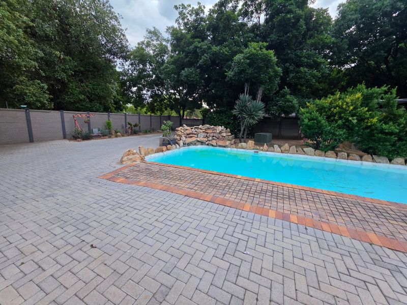 Outdoor pool area featuring a rock water feature, surrounded by extensive paved patio space and a secure boundary wall.