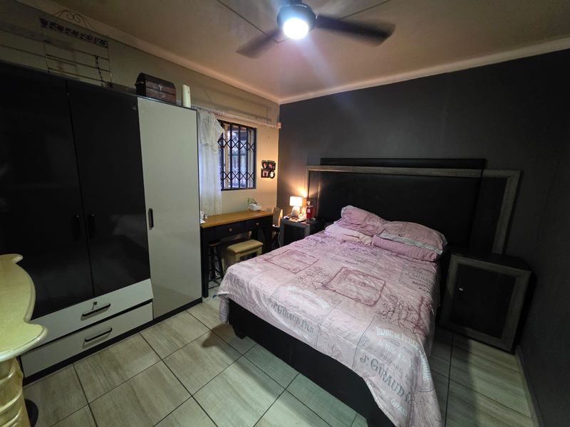 A functional bedroom featuring tiled flooring, a ceiling fan, and built-in wardrobe storage with security bars on the window.