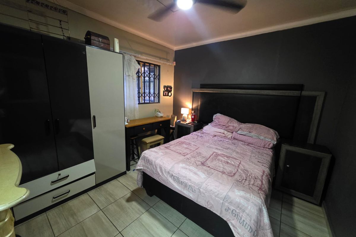 A functional bedroom featuring tiled flooring, a ceiling fan, and built-in wardrobe storage with security bars on the window.