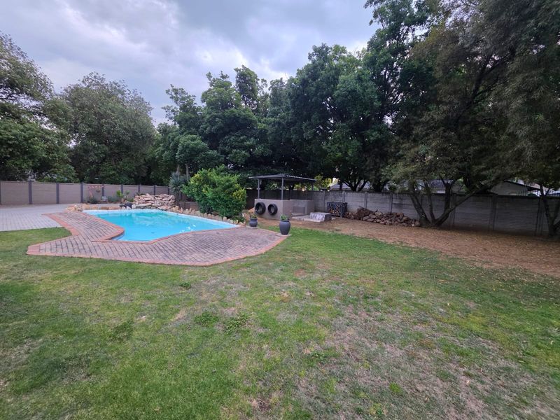 Spacious backyard featuring a swimming pool with paved surround, a built-in braai area, and established perimeter walling.