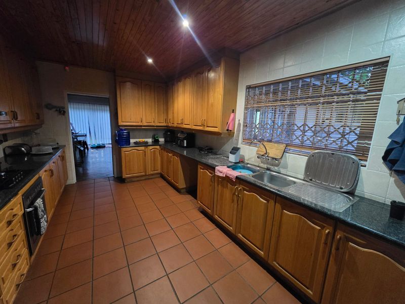 A functional kitchen featuring wooden cabinetry, granite countertops, a stainless steel sink, and tiled flooring with a warm timber ceiling finish.