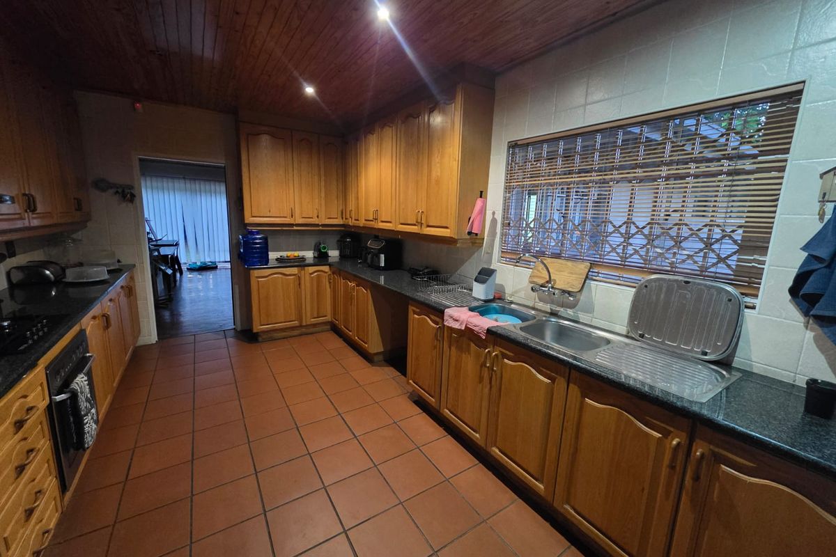 A functional kitchen featuring wooden cabinetry, granite countertops, a stainless steel sink, and tiled flooring with a warm timber ceiling finish.