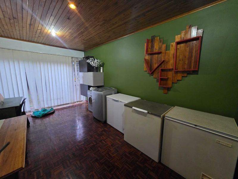 A functional laundry area featuring parquet flooring, a timber-paneled ceiling, and vertical blinds leading to an outdoor space.
