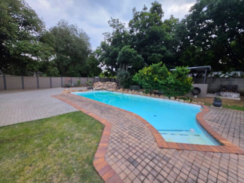 Outdoor pool area featuring a swimming pool with paved surround, rock feature, and perimeter boundary wall.