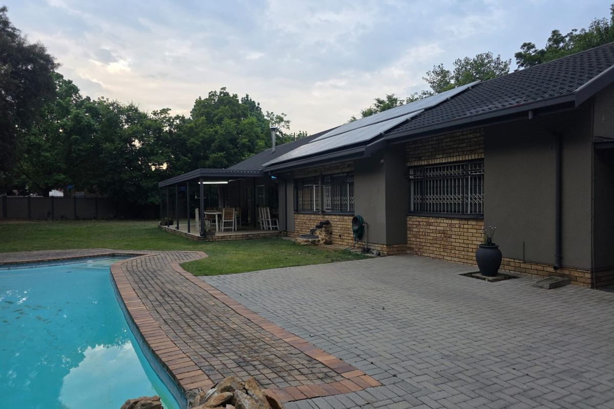 Rear exterior view featuring a swimming pool, paved patio area, covered veranda, and solar panels installed on the roof.