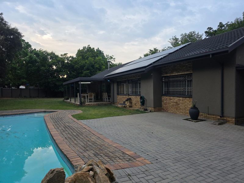 Rear exterior view featuring a swimming pool, paved patio area, covered veranda, and solar panels installed on the roof.