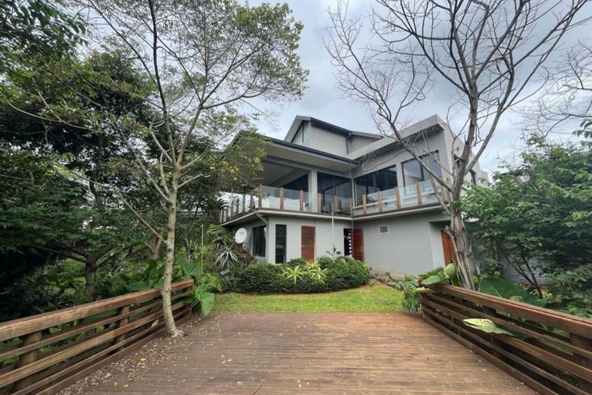 A modern multi-level home featuring a spacious timber deck, glass balustrades, and a covered balcony overlooking a lush, landscaped garden.