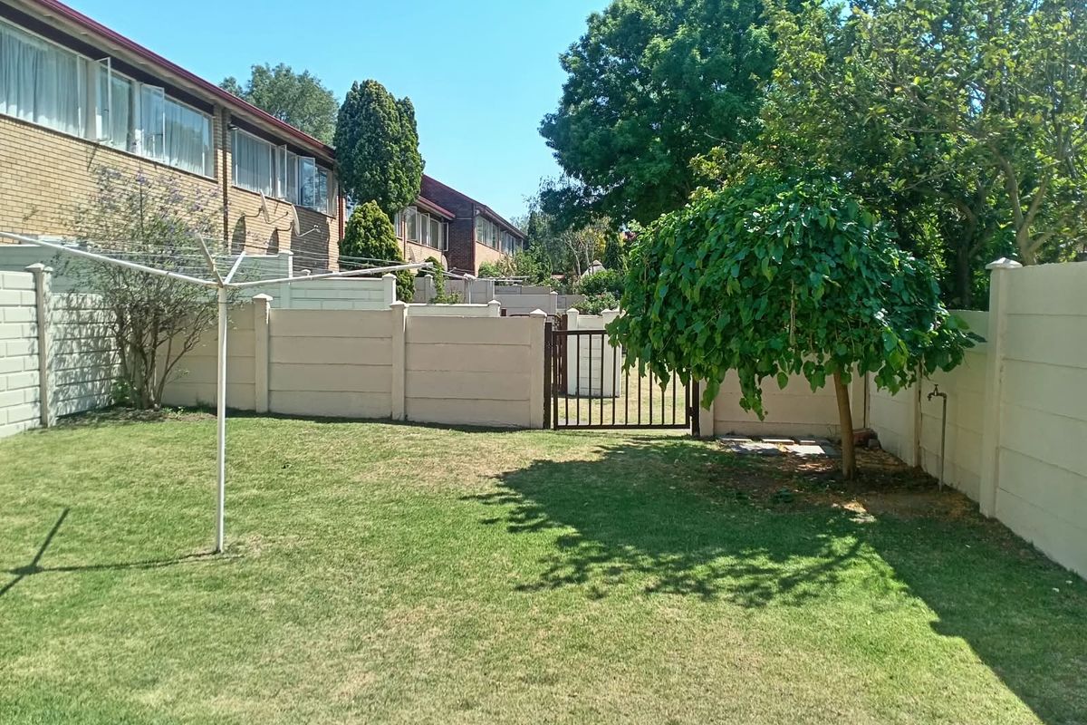 A private rear garden featuring a well-maintained lawn, precast concrete boundary walls, a secure metal pedestrian gate, and a rotary clothesline.