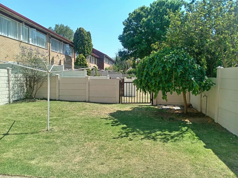 A private rear garden featuring a well-maintained lawn, precast concrete boundary walls, a secure metal pedestrian gate, and a rotary clothesline.