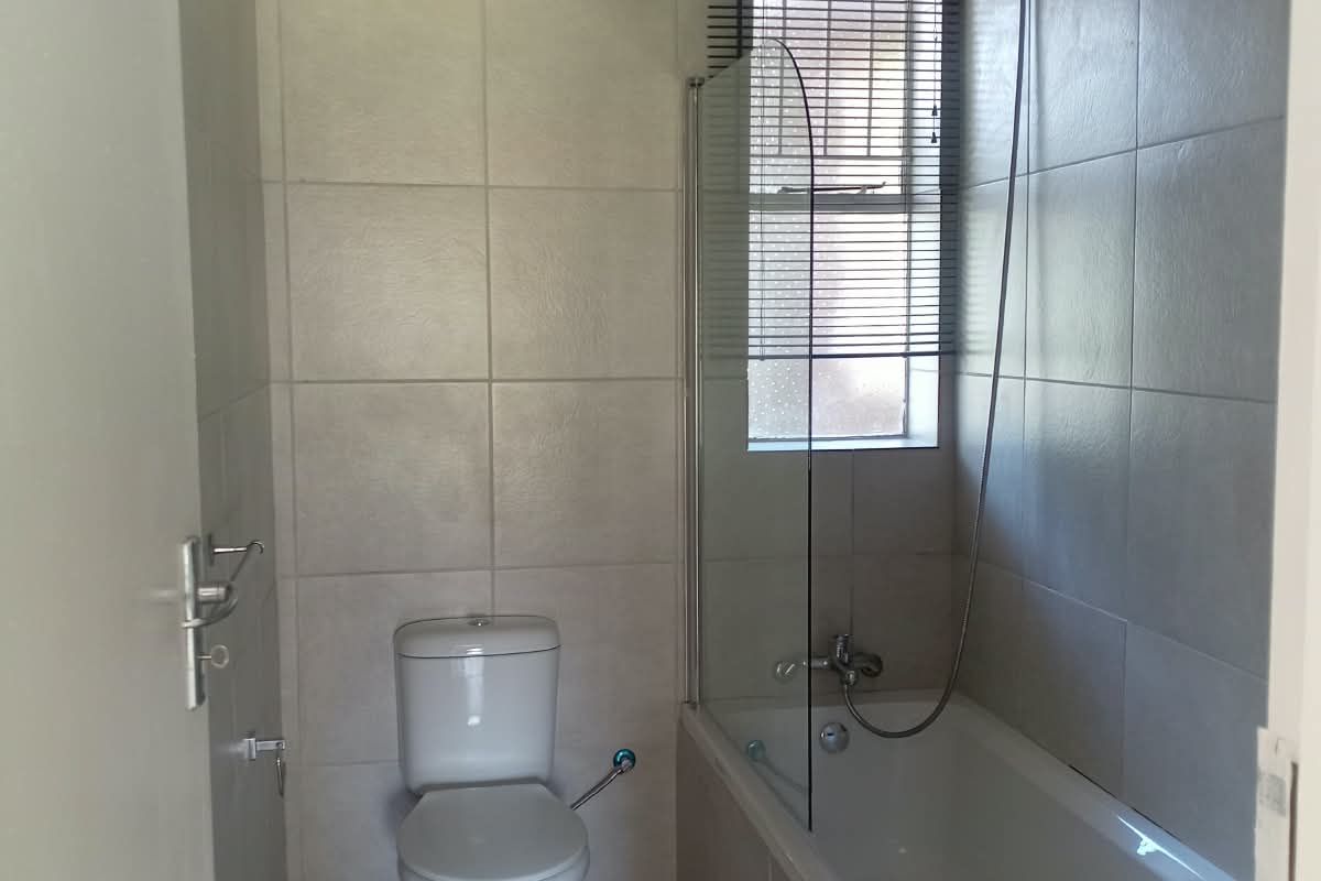 A functional bathroom featuring a bathtub with a glass shower screen, a toilet, and neutral wall and floor tiling.