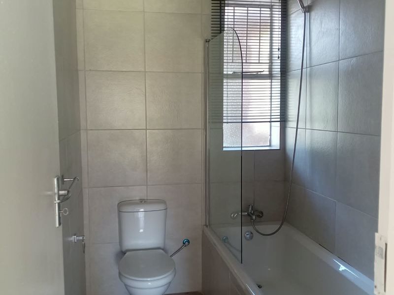 A functional bathroom featuring a bathtub with a glass shower screen, a toilet, and neutral wall and floor tiling.