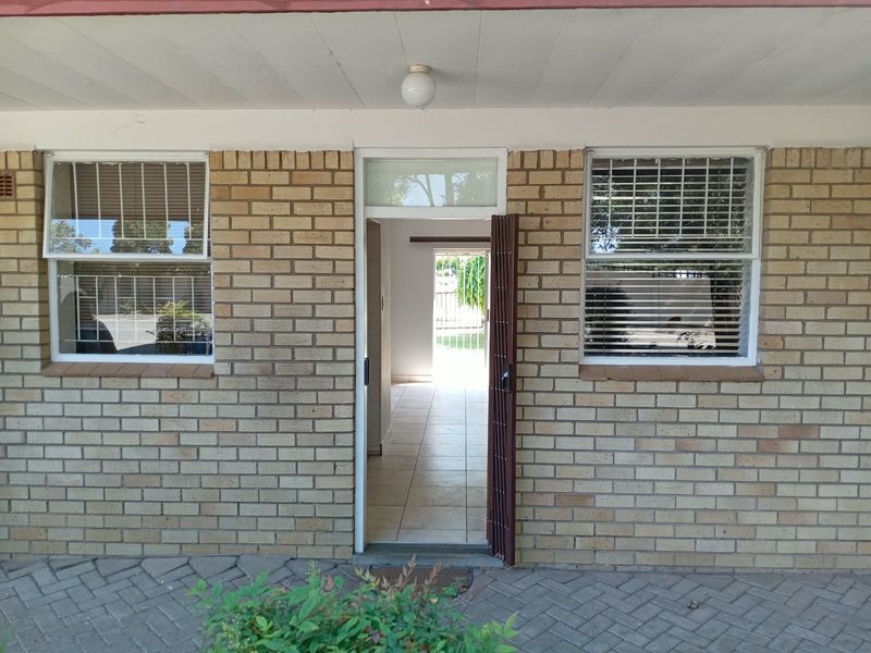 Front entrance of the apartment featuring a brick facade, security gate, and tiled entryway with clear views through to the rear garden.